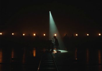 Movie still from “This Much I Know to Be True” (2022), directed by Andrew Dominik – A man sitting on a train track in the dark; Extreme Wide shot, High angle