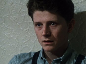 Movie still from “Threads” (1984), directed by Mick Jackson – A young man in a blue checkered dress shirt and suspenders; Close Up shot, Low angle