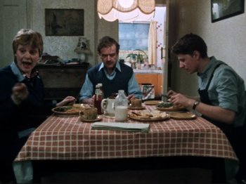Movie still from “Threads” (1984), directed by Mick Jackson – A group of people sitting at a table with food; Wide shot, High angle
