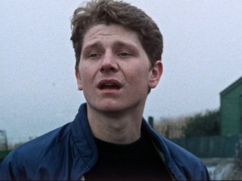 Movie still from “Threads” (1984), directed by Mick Jackson – A young man with short brown hair wearing a blue jacket; Close Up shot, High angle