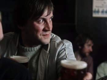 Movie still from “Threads” (1984), directed by Mick Jackson – A man sitting in front of two other people drinking beer; Medium shot, Low angle