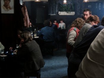 Movie still from “Threads” (1984), directed by Mick Jackson – A group of people sitting at tables in a room; Wide shot, Over the shoulder angle