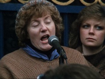 Movie still from “Threads” (1984), directed by Mick Jackson – An older woman is speaking into a microphone; Close Up shot, Over the shoulder angle
