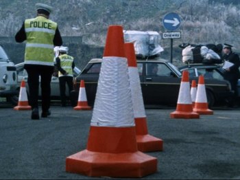 Movie still from “Threads” (1984), directed by Mick Jackson – A police officer standing in front of a group of traffic cones; Wide shot, High angle