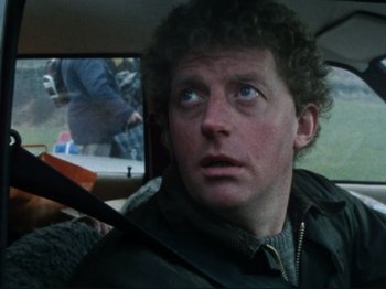 Movie still from “Threads” (1984), directed by Mick Jackson – A person sitting in a car holding a baseball bat; Close Up shot, Over the shoulder angle