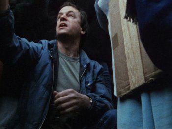Movie still from “Threads” (1984), directed by Mick Jackson – A man in a blue jacket is sitting on the ground; Close Up shot, Low angle