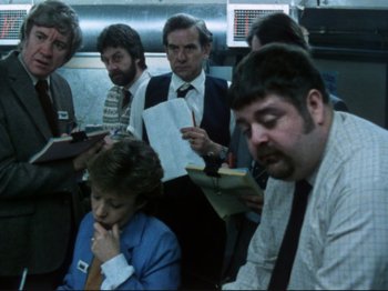 Movie still from “Threads” (1984), directed by Mick Jackson – A group of people sitting in a room; Medium shot, High angle