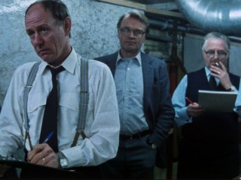 Movie still from “Threads” (1984), directed by Mick Jackson – A group of men standing next to each other in a room; Medium shot, Low angle