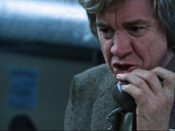 Movie still from “Threads” (1984), directed by Mick Jackson – An older man talking on a phone while wearing a suit and tie; Close Up shot, Low angle