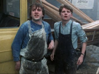 Movie still from “Threads” (1984), directed by Mick Jackson – Two young men standing next to each other in front of a building; Medium shot, Low angle