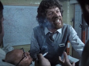 Movie still from “Threads” (1984), directed by Mick Jackson – A man smoking a cigarette while another man looks on; Medium shot, Over the shoulder angle