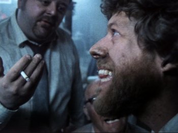 Movie still from “Threads” (1984), directed by Mick Jackson – A man with a beard is smoking a cigarette while another man looks on; Close Up shot, Low angle