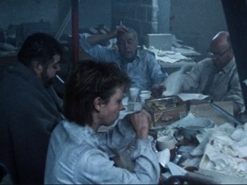 Movie still from “Threads” (1984), directed by Mick Jackson – A group of people sitting at a table with papers; Wide shot, High angle