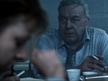 Movie still from “Threads” (1984), directed by Mick Jackson – An older man sitting at a table with a cup of coffee in front of him; Close Up shot, Over the shoulder angle