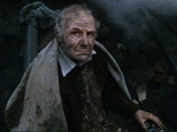 Movie still from “Threads” (1984), directed by Mick Jackson – An old man with a beard is holding a knife; Medium shot, High angle