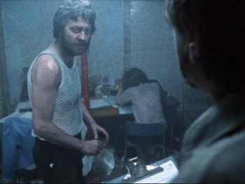 Movie still from “Threads” (1984), directed by Mick Jackson – A man standing in front of a mirror in a room; Medium shot, Low angle