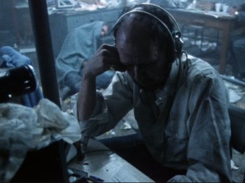 Movie still from “Threads” (1984), directed by Mick Jackson – An older man wearing headphones sitting at a table; Medium shot, High angle