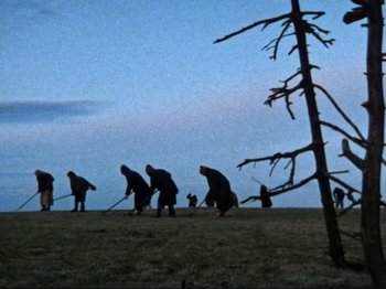 Movie still from “Threads” (1984), directed by Mick Jackson – A group of people standing on top of a grass covered field; Extreme Wide shot, Low angle