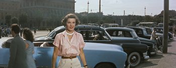 Movie still from “Three Coins in the Fountain” (1954), directed by Jean Negulesco – A woman standing in a parking lot next to parked cars; Medium shot, Low angle
