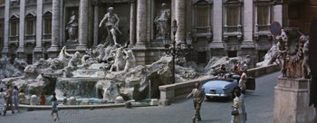 Movie still from “Three Coins in the Fountain” (1954), directed by Jean Negulesco – A man walking down a street near a fountain; Extreme Wide shot, High angle