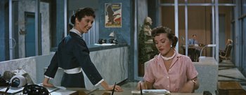 Movie still from “Three Coins in the Fountain” (1954), directed by Jean Negulesco – Two women are sitting at a table and one of the women is holding a pen; Medium shot, Over the shoulder angle