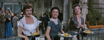 Movie still from “Three Coins in the Fountain” (1954), directed by Jean Negulesco – A woman holding a plate of food in a restaurant; Medium shot, Low angle