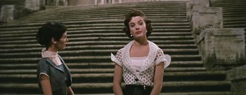 Movie still from “Three Coins in the Fountain” (1954), directed by Jean Negulesco – A woman standing on some steps wearing a white blouse; Medium shot, Low angle