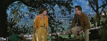 Movie still from “Three Coins in the Fountain” (1954), directed by Jean Negulesco – A woman in a yellow polka dot dress standing next to a man in an orange jacket; Medium shot, High angle
