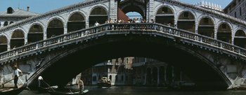 Movie still from “Three Coins in the Fountain” (1954), directed by Jean Negulesco – A bridge over a river with people on it and boats in the water; Extreme Wide shot, High angle
