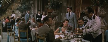 Movie still from “Three Coins in the Fountain” (1954), directed by Jean Negulesco – A group of people sitting at a table with wine glasses; Medium shot, Over the shoulder angle