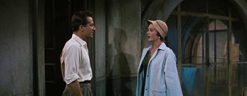 Movie still from “Three Coins in the Fountain” (1954), directed by Jean Negulesco – A man and a woman standing next to each other in front of a building; Medium shot, Over the shoulder angle