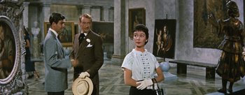 Movie still from “Three Coins in the Fountain” (1954), directed by Jean Negulesco – A man and a woman standing next to each other in front of paintings; Medium shot, Over the shoulder angle