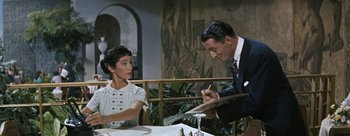 Movie still from “Three Coins in the Fountain” (1954), directed by Jean Negulesco – A man and a woman sitting at a dinner table; Medium shot, Over the shoulder angle