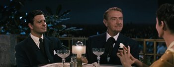 Movie still from “Three Coins in the Fountain” (1954), directed by Jean Negulesco – A man sitting at a dinner table holding a flower; Medium shot, Over the shoulder angle