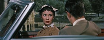 Movie still from “Three Coins in the Fountain” (1954), directed by Jean Negulesco – A woman in a hat sitting next to a man in the back of a car; Close Up shot, Over the shoulder angle