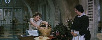 Movie still from “Three Coins in the Fountain” (1954), directed by Jean Negulesco – A woman sitting at a table with a basket of flowers; Medium shot, Low angle