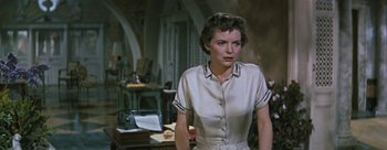 Movie still from “Three Coins in the Fountain” (1954), directed by Jean Negulesco – A woman standing in front of a table in a room; Medium shot, Low angle