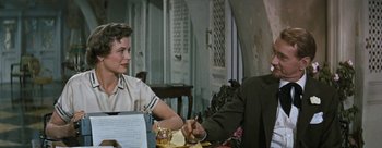 Movie still from “Three Coins in the Fountain” (1954), directed by Jean Negulesco – A woman sitting at a dinner table with a man; Medium shot, High angle