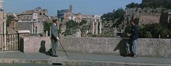 Movie still from “Three Coins in the Fountain” (1954), directed by Jean Negulesco – A man in a suit and hat is holding a cane and looking out at the ruins; Wide shot, Low angle