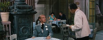 Movie still from “Three Coins in the Fountain” (1954), directed by Jean Negulesco – An older man sitting at a table in front of other people; Medium shot, Over the shoulder angle