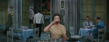 Movie still from “Three Coins in the Fountain” (1954), directed by Jean Negulesco – A woman sitting at a table drinking a beverage; Medium shot, High angle