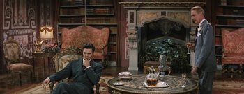 Movie still from “Three Coins in the Fountain” (1954), directed by Jean Negulesco – A man sitting in a chair in front of a fireplace; Wide shot, High angle