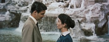 Movie still from “Three Coins in the Fountain” (1954), directed by Jean Negulesco – A man and a woman standing next to each other in front of a fountain; Medium shot, Over the shoulder angle