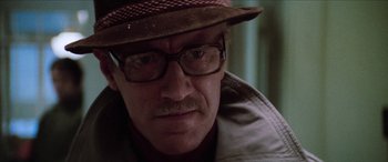 Movie still from “Three Days of the Condor” (1975), directed by Sydney Pollack – A person wearing glasses and a hat; Close Up shot, Over the shoulder angle