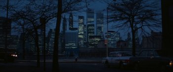 Movie still from “Three Days of the Condor” (1975), directed by Sydney Pollack – A car parked on the side of the road in front of a large city; Extreme Wide shot, High angle
