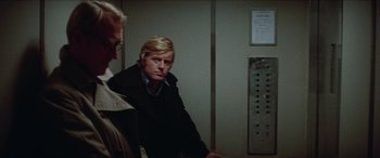 Movie still from “Three Days of the Condor” (1975), directed by Sydney Pollack – A man with blonde hair sitting next to another man; Medium shot, Low angle