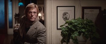 Movie still from “Three Days of the Condor” (1975), directed by Sydney Pollack – A man in a suit and glasses in front of a picture; Medium shot, Over the shoulder angle