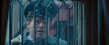 Movie still from “Three Days of the Condor” (1975), directed by Sydney Pollack – A man in a police uniform behind a fence; Close Up shot, Over the shoulder angle