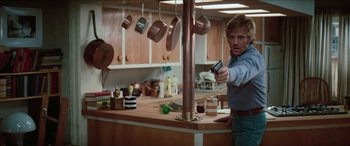 Movie still from “Three Days of the Condor” (1975), directed by Sydney Pollack – A man holding a gun while standing in a kitchen; Medium shot, Low angle