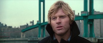 Movie still from “Three Days of the Condor” (1975), directed by Sydney Pollack – A person wearing a jacket near a bridge; Close Up shot, Low angle